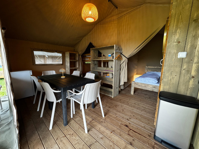Innenraum eines Safarizeltes mit Holzboden, Esstisch, Stühlen, Kühlschrank und Betten.