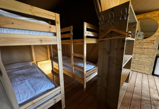 Interno di una tenda safari con due letti a castello in legno, scaffali, appendiabiti e specchio tondo.