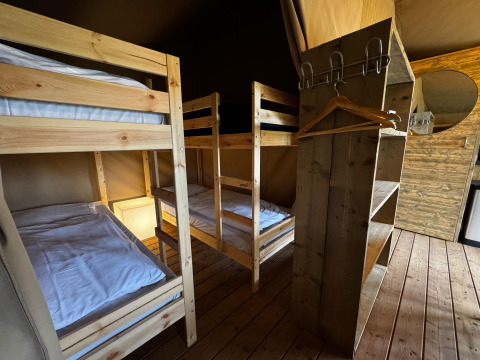 Intérieur d’une tente safari avec deux lits superposés en bois, étagères, cintres et miroir rond.