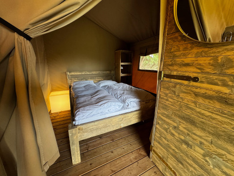 Vista interior de una tienda safari con cama doble, muebles de madera y luz ambiental suave.