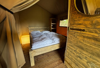 Vista interior de una tienda safari con cama doble, muebles de madera y luz ambiental suave.