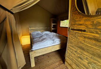 Vista interior de una tienda safari con cama doble, muebles de madera y luz ambiental suave.