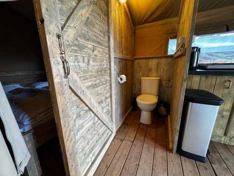 Interior view of a safari tent at Maasduinen in the Netherlands showing toilet, bed, and rustic wood.