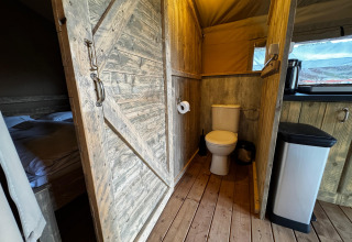 Indvendigt billede af et safari telt ved Maasduinen med toilet, seng og træinteriør i Nederlandene.