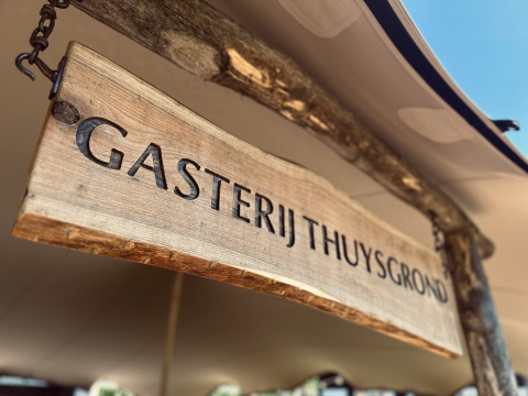 Træskilt med teksten 'Gasterij Thuysgrond' på et feriested i Noord-Brabant, Holland, under solrigt telt.