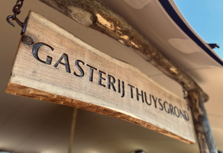 Træskilt med teksten 'Gasterij Thuysgrond' på et feriested i Noord-Brabant, Holland, under solrigt telt.
