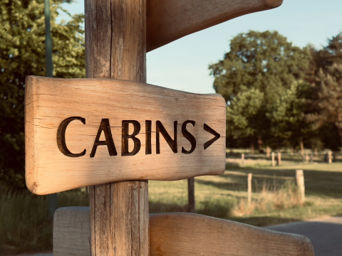 Cartello in legno con scritto 'CABINS>' al parco vacanze Thuysgrond, North Brabant, Paesi Bassi, alberi sullo sfondo.