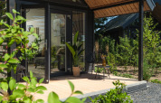 Moderne Sommerlodge mit Glastür und Holzterrasse im grünen Freizeitpark Rhederlaagse Meren, Niederlande.