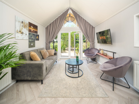 Sommer Lodge stue ved Rhederlaagse Meren, med moderne sofa, stole, kunstværker og udsigt til haven.
