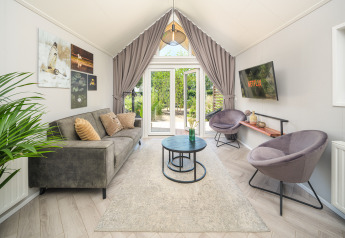 Sommer Lodge stue ved Rhederlaagse Meren, med moderne sofa, stole, kunstværker og udsigt til haven.