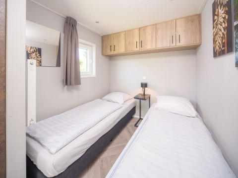 Chambre claire du Summer Lodge avec deux lits simples, fenêtre, placards en bois et table de chevet.