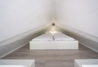 Dormitorio abuhardillado con techo bajo y cama doble en Summer Lodge, Parque y Marina Rhederlaagse Meren, Países Bajos.