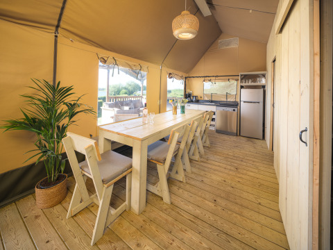 Interieur van Safari tent Ranger met eettafel, houten stoelen en keuken bij Rhederlaagse Meren, Nederland.