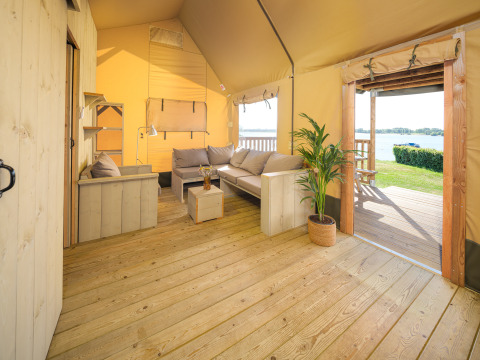 Interior de la tienda Safari Ranger con suelo de madera, sofás y vista al lago en Rhederlaagse Meren, Países Bajos.