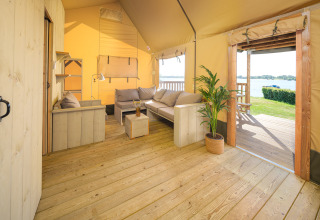 Interior de la tienda Safari Ranger con suelo de madera, sofás y vista al lago en Rhederlaagse Meren, Países Bajos.