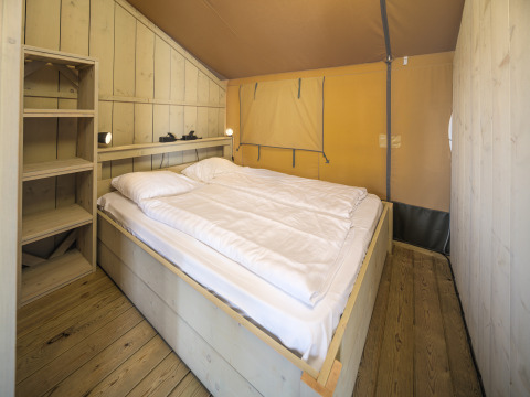Binnenaanzicht van de Safari tent Ranger met tweepersoonsbed en planken in recreatiepark Rhederlaagse Meren.