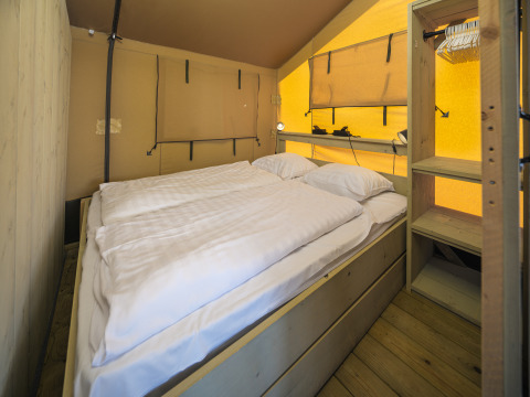 Innenansicht des Safari-Zelts Ranger im Rhederlaagse Meren, Niederlande, mit Doppelbett und Holzregalen.