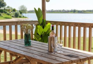 Mesa de madera con vino, copas y un jarrón, en una terraza con vista al lago en los Países Bajos.