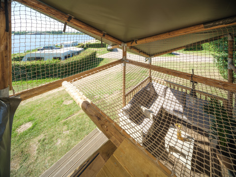 Blick von einem Safari-Zelt mit Netz und Sitzbereich auf den Campingplatz und das Wasser bei Rhederlaagse Meren.