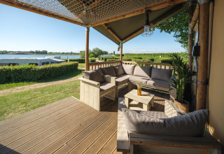 Zona de estar exterior de la Safari tent Ranger con sofás y vistas a la marina en Rhederlaagse Meren, Países Bajos.