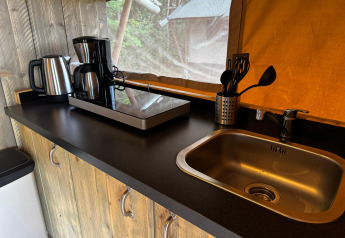 Kitchen counter in a safari tent with electric kettle, coffee maker, hob, utensils and a metal sink.
