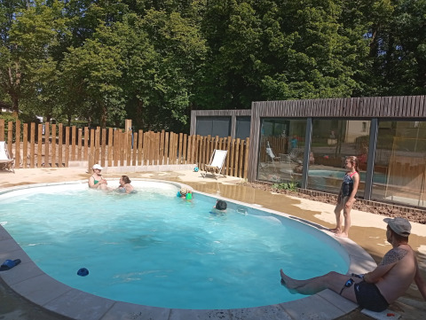 Famiglie e bambini si rilassano nella piscina all’aperto al Camping Seasonova Vittel, circondati da alberi.
