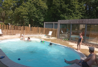Børn og voksne nyder udendørs swimmingpool på Camping Seasonova Vittel, omgivet af træer og solskin.