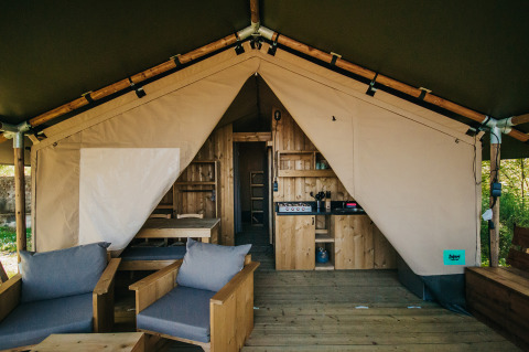 Interior of a safari tent with wooden furniture, kitchenette, and bathroom facilities at Camping Lucherino, Italy.