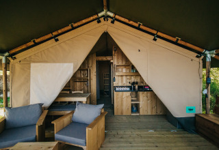 Interior of a safari tent with wooden furniture, kitchenette, and bathroom facilities at Camping Lucherino, Italy.