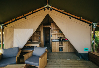 Interieur van een safaritent met houten meubilair, keuken en sanitair op Camping Lucherino in Italië.