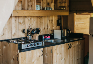Wooden kitchenette with gas stove and shelving inside a safari tent at Camping Lucherino, Italy.