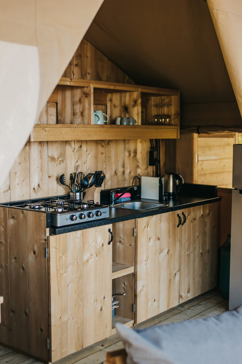 Wooden kitchenette with gas stove and shelving inside a safari tent at Camping Lucherino, Italy.