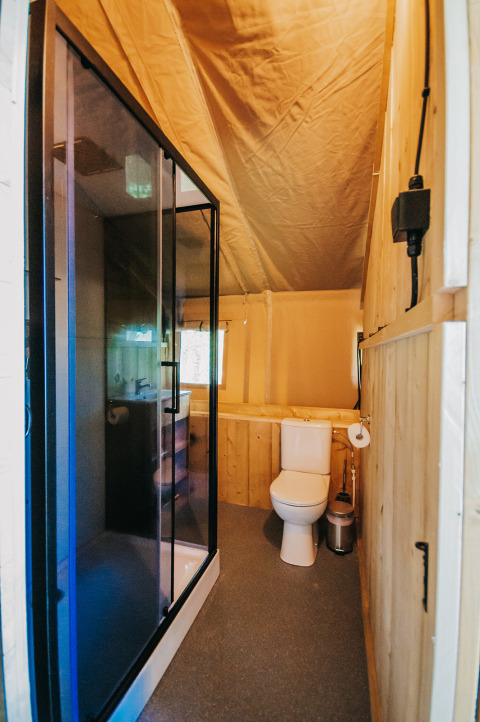 Badkamer in safaritent met douche en toilet bij Camping Lucherino in Italië, warm interieur.