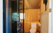 Salle de bain dans une tente safari avec douche et toilettes au Camping Lucherino en Italie, ambiance cosy.