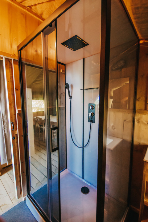 Modern shower cabin inside a luxury safari tent with wooden walls at Camping Lucherino in Italy.