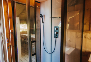 Cabina de ducha moderna dentro de una tienda safari de lujo con paredes de madera en Camping Lucherino, Italia.