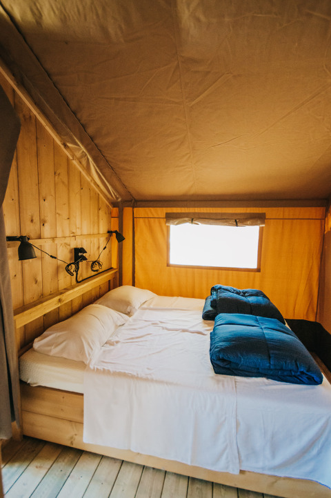 Interior view of a safari tent with double bed and wood walls at Camping Lucherino in Italy.