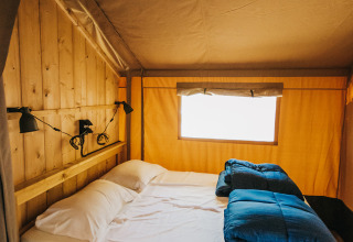 Interior view of a safari tent with double bed and wood walls at Camping Lucherino in Italy.