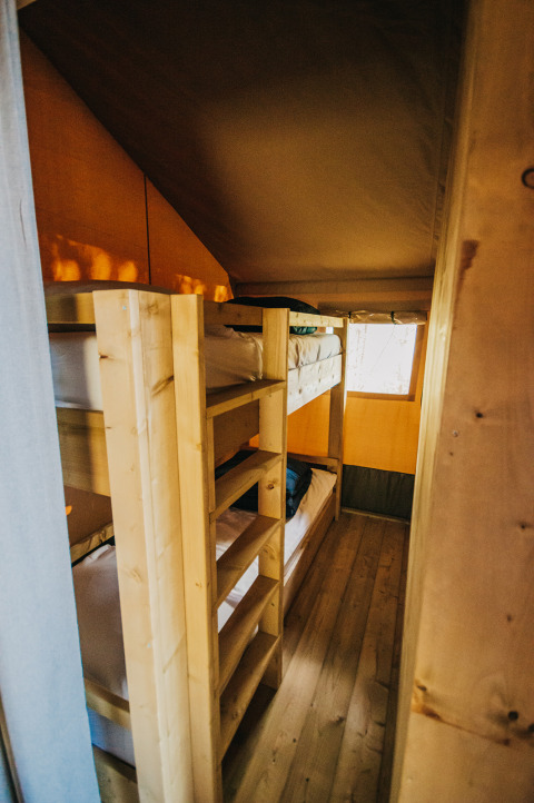 Interieur van safaritent met houten stapelbedden en houten vloer bij Camping Lucherino in Italië.