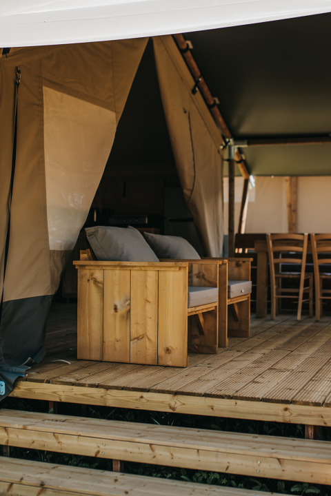 Wooden furniture and seating on the terrace of a safari tent at Camping Lucherino in Italy, relaxing vibe.