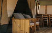 Træmøbler og siddepladser på terrassen i et safaritelt ved Camping Lucherino i Italien, afslappet stemning.