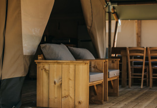 Muebles de madera y zona de estar en la terraza de una tienda safari en Camping Lucherino, Italia, ambiente relajado.