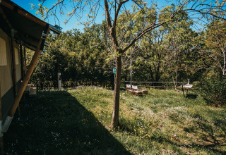 Safari-Zelt Garten beim Camping Lucherino in Italien mit Bäumen, Wiese und gemütlicher Sitzgelegenheit.