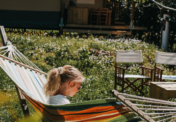 Niña descansando en una colorida hamaca frente a una tienda safari en Camping Lucherino, Italia, primavera.