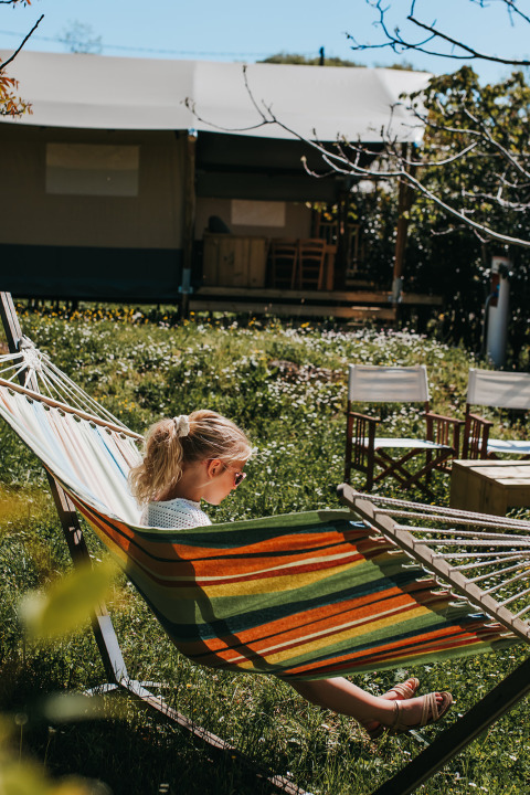 Girl relaxing in a colorful hammock in front of a safari tent at Camping Lucherino, Italy, springtime.