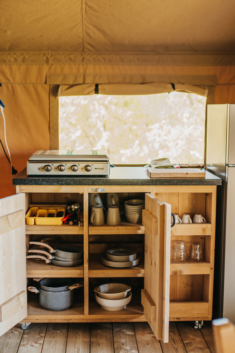 Cocina de camping en Safari Tent Garden, Camping Lucherino, Italia, con armarios abiertos y utensilios visibles.