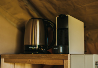 Elkedel og kaffemaskine på en træhylde inde i Safari Tent Garden på Camping Lucherino i Italien.