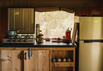 Küchenbereich im Safari-Zelt mit Holzschrank, Gasherd, Tassen und Kühlschrank, Camping Lucherino.