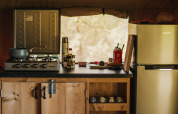 Kitchen space in a safari tent at Camping Lucherino, Italy, with stove, wooden cabinets and fridge.