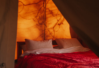 Indersiden af et Safari Tent Garden på Camping Lucherino i Italien med en hyggelig seng og dæmpet lys.